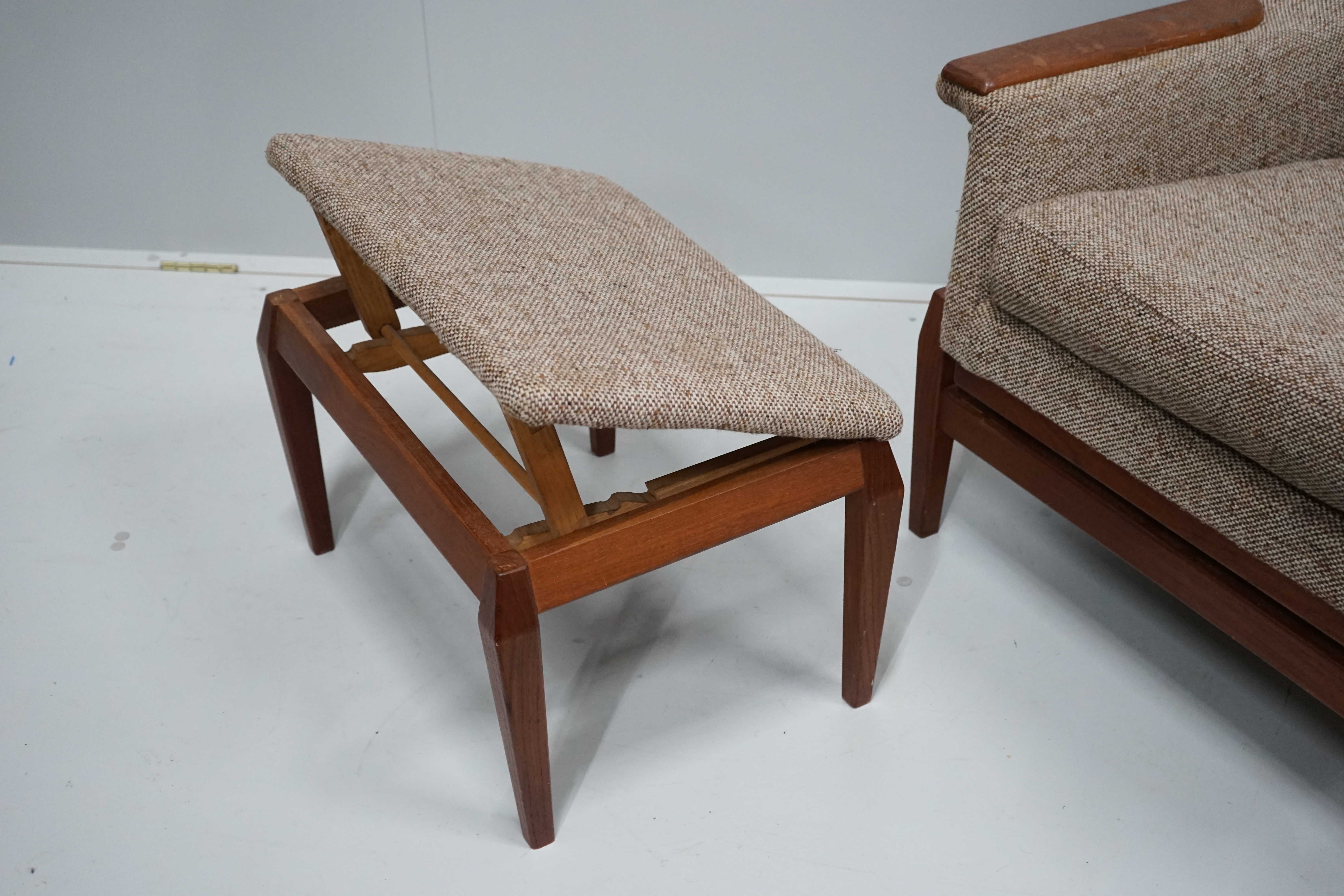 In the manner of Kofod Larsen, a mid century upholstered teak reclining armchair and adjustable foot stool, chair width 87cm, depth 86cm, height 102cm.